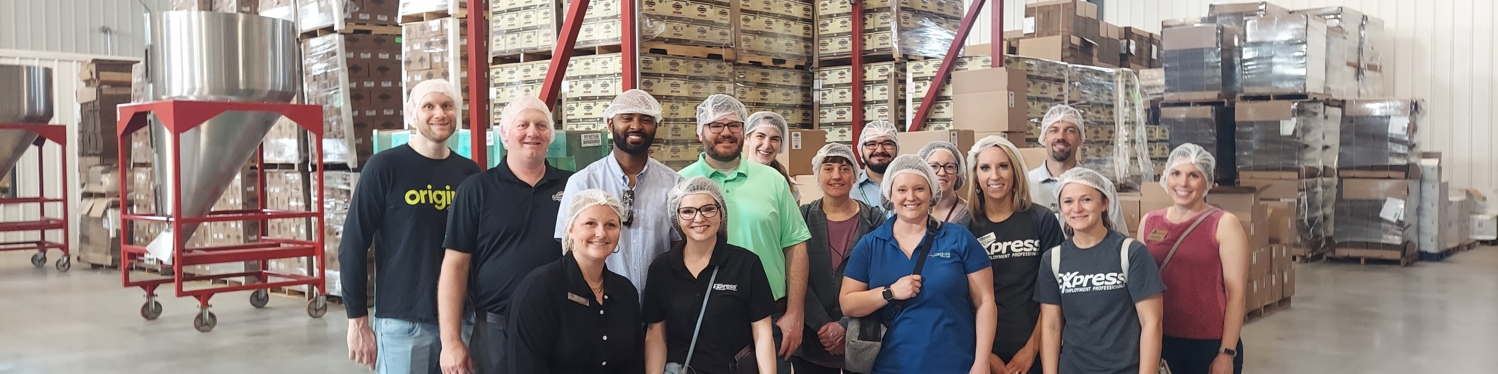 group of people in hairnets in front of stacked boxes of coffee.