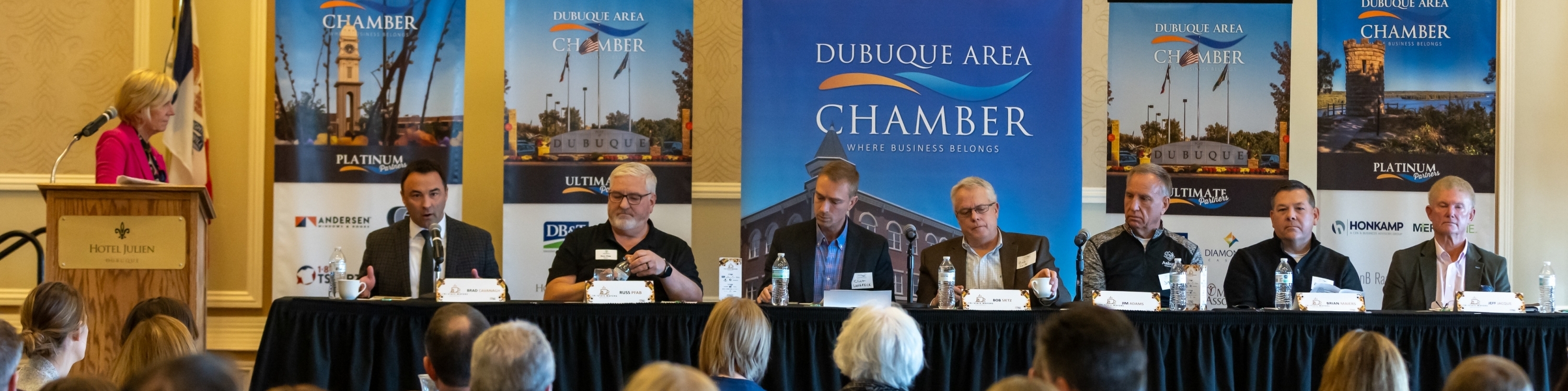 row of people at tables with banners of Dubuque behind them
