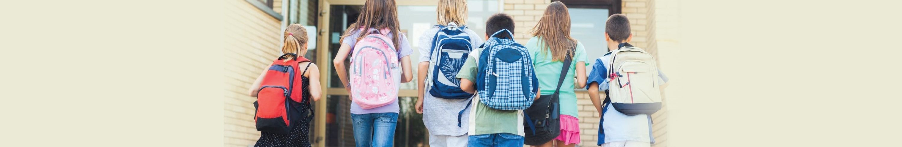 kids wearing backpacks walking into a school
